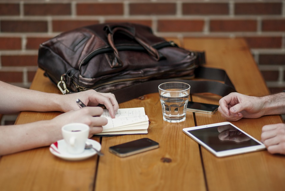 Two people sitting at a table with coffee and cell phones.