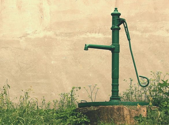 A green water pump sitting on top of a tree stump.